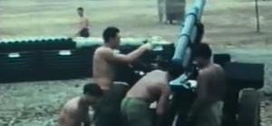 Four shirtless men in green military trousers grouped around a artillery gun