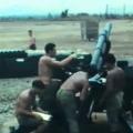 Four shirtless men in green military trousers grouped around a artillery gun
