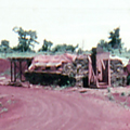 Military structures set amongst red soil with green grass and jungle in the background