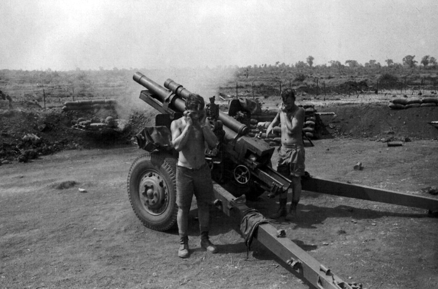 Black and white photograph of two men standing to next to artillery gun as it is fired