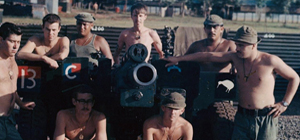 Group of men in khaki military uniform standing and kneeling around artillery gun.