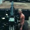 Shirtless man standing next to artillery gun