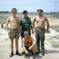 Four men, three shirtless, grouped together in military uniform.